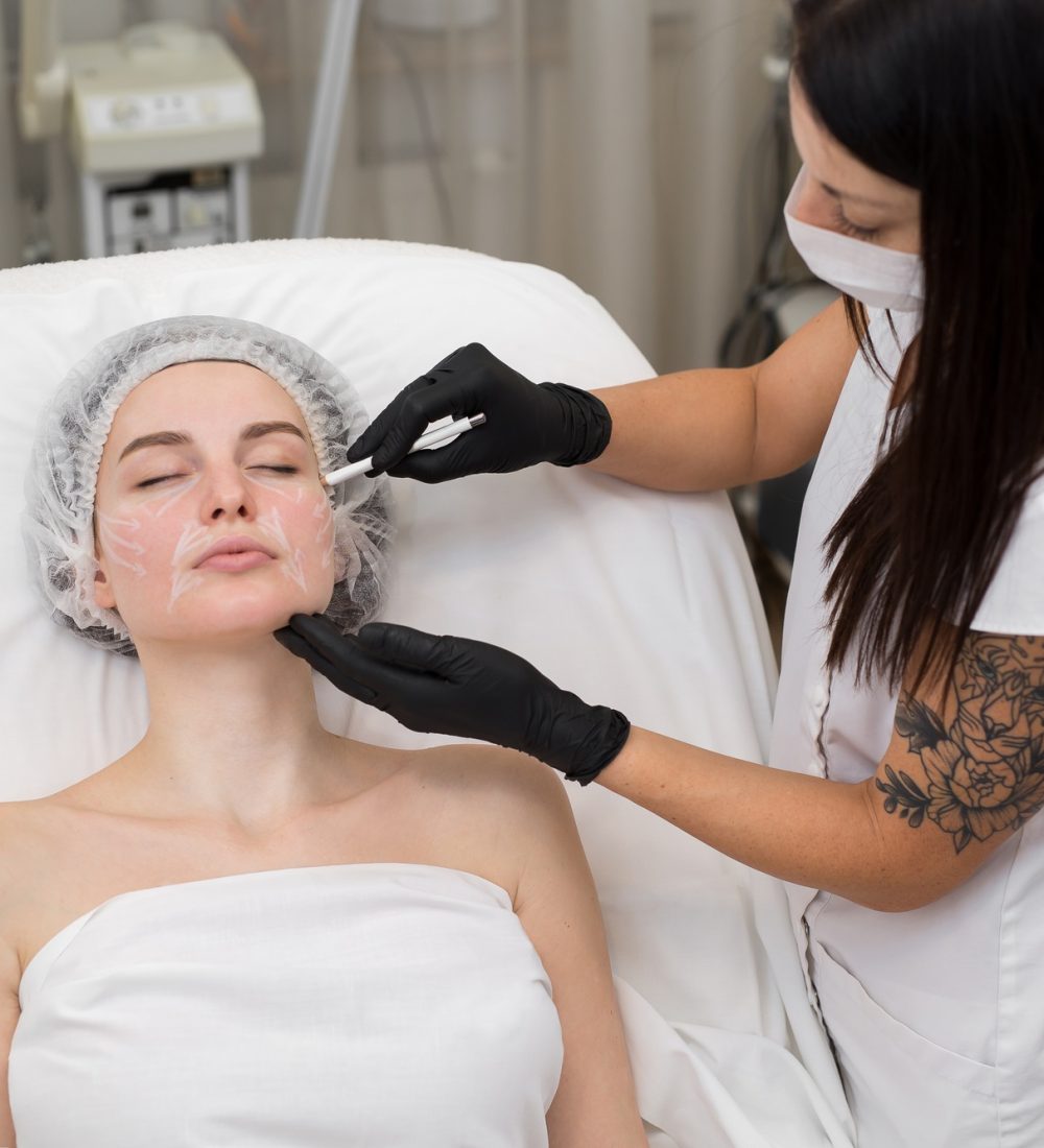 Beautician draws the contours of a white pencil on the face of the patient.